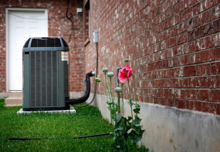 Air conditioning unit beside flowering plants in a residential backyard, highlighting energy-efficient HVAC solutions relevant to SEER ratings.